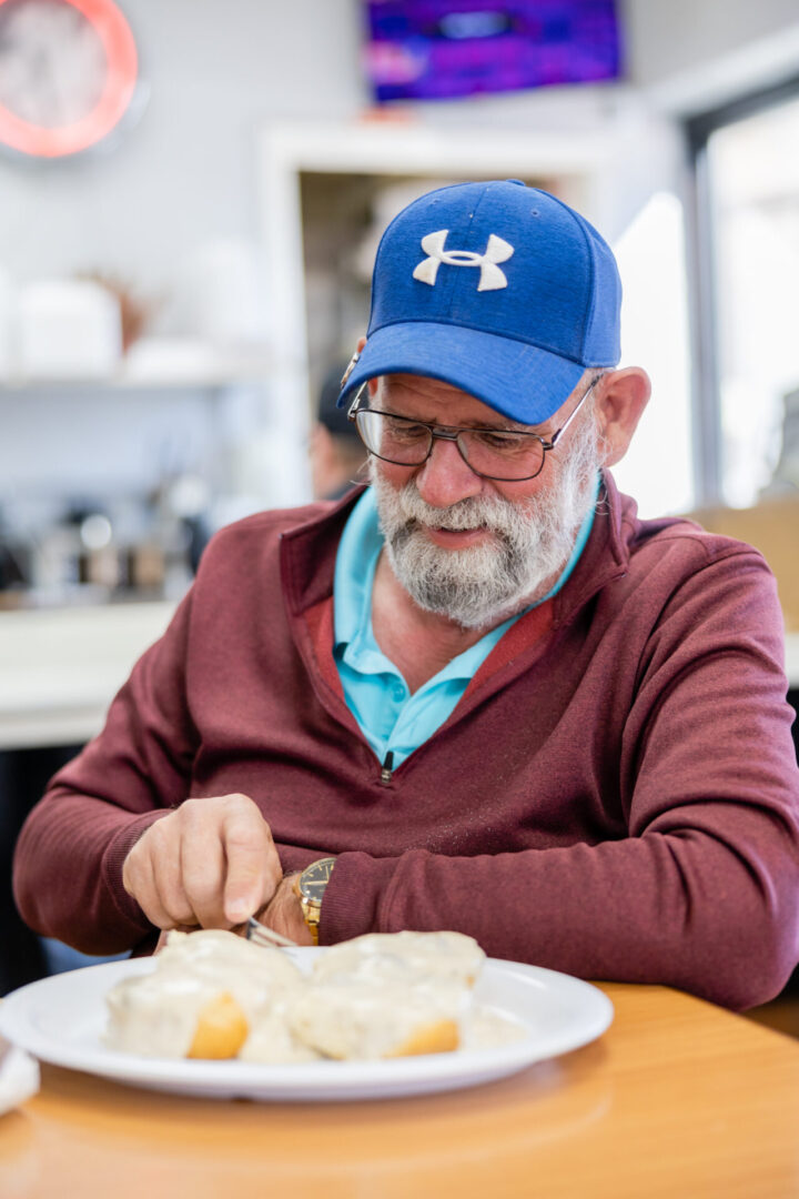 A man in a blue hat is cutting food.